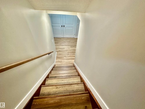 Staircase with wood-finish treads and a wall-mounted cylindrical handrail, complemented by double doors featuring recessed panels - 4723 105 Street Nw, Edmonton, AB 