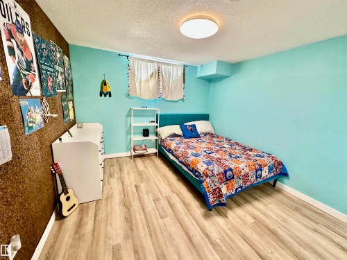 Room featuring wood-finish flooring, a cork-textured accent wall, and a flush-mount overhead light fixture - 4723 105 Street Nw, Edmonton, AB 