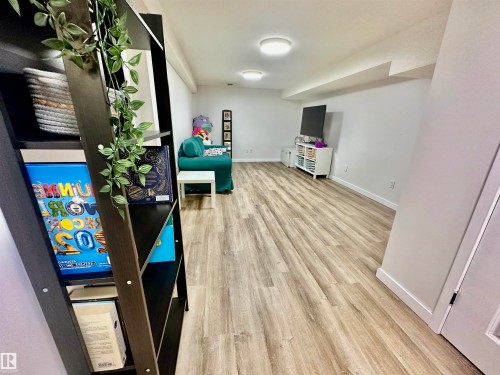 Expansive room featuring wood-finish flooring, neutral wall paint, and dual flush-mount ceiling light fixtures - 4723 105 Street Nw, Edmonton, AB 
