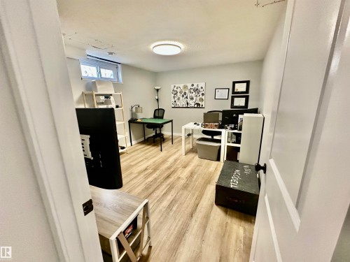Interior room featuring wood-finish flooring, neutral wall paint, a flush-mount circular light fixture, and a rectangular egress window - 4723 105 Street Nw, Edmonton, AB 