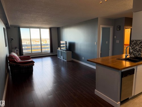 Open-concept interior featuring wood-finish flooring, floor-to-ceiling sliding glass doors, kitchen island with a wood countertop, and a herringbone-patterned tile backsplash - #1304 10160 116 St Nw, Edmonton, AB 