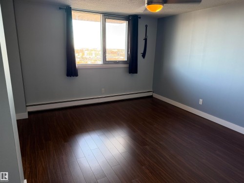 Room featuring wood-finish flooring, a large window, and an attached ceiling fan with lighting - #1304 10160 116 St Nw, Edmonton, AB 