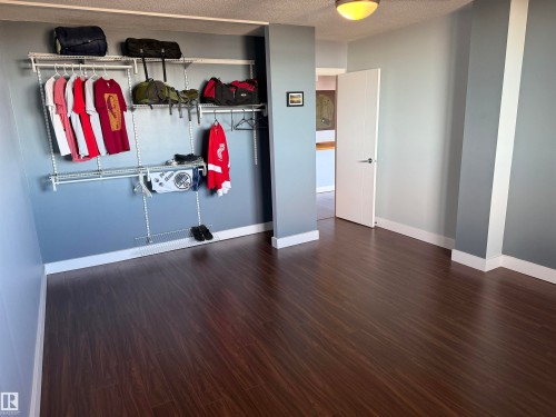 Room featuring dark wood-finish flooring, a wall-mounted wire storage system, and a flush-mount ceiling light fixture - #1304 10160 116 St Nw, Edmonton, AB 