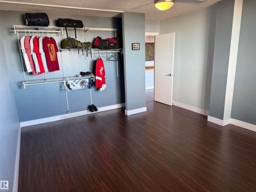 Room featuring dark wood-finish flooring, white flush-mount ceiling light fixture, neutral wall paint, and white interior door with brushed metal hardware - #1304 10160 116 St Nw, Edmonton, AB 
