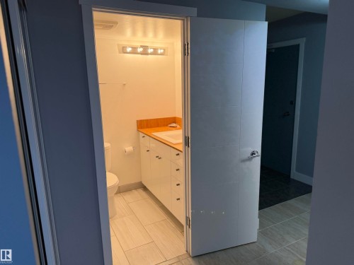 Bathroom featuring a glossy white vanity with integrated sink, wood-finish countertop, linear multi-bulb light fixture, and tile flooring - #1304 10160 116 St Nw, Edmonton, AB 