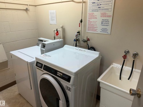 Laundry area featuring white stackable commercial appliances and a utility sink with dual-faucet plumbing - #1304 10160 116 St Nw, Edmonton, AB 