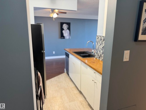 Kitchen featuring white flat-panel cabinetry, wood-tone countertops, a dark-finish drop-in sink with a high-arch faucet, and a decorative herringbone-pattern backsplash - #1304 10160 116 St Nw, Edmonton, AB 