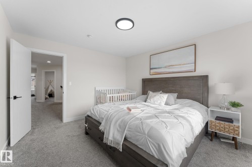 Spacious bedroom featuring light neutral wall tones, grey carpeting, a flush-mount ceiling light, and a solid wood headboard - 1142 Goldfinch Crescent Nw, Edmonton, AB 