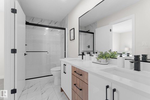 Dual vanity with integrated sinks and black matte faucets, wood-finish and white cabinetry, a large frameless mirror, and a glass-enclosed shower with a black matte frame - 1142 Goldfinch Crescent Nw, Edmonton, AB 