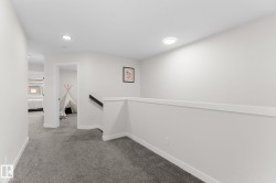 Recessed ceiling lighting illuminates the gray carpeted hallway with white painted walls - 
