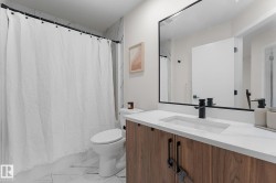 White tile flooring, wood-finish vanity with dual-handle fixtures, white countertop with integrated sink, black-framed mirror, and white shower curtain with black rod - 