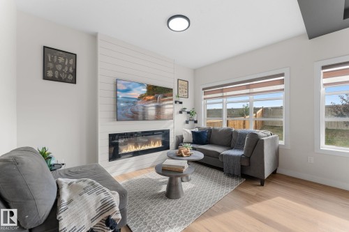 Shiplap accent wall with an electric fireplace, wood-finish flooring, recessed ceiling lighting, and multiple windows - 1142 Goldfinch Crescent Nw, Edmonton, AB 