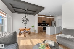 Coffered ceiling with a modern chandelier, wood-finish flooring, and a kitchen featuring wood-grain cabinetry, stainless steel appliances, and a central island - 