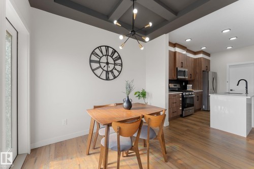 Coffered ceiling with modern chandelier, wood-finish flooring, white kitchen island with sink, stainless steel appliances, and wood-finish cabinetry - 1142 Goldfinch Crescent Nw, Edmonton, AB 