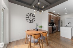 Coffered ceiling with modern chandelier, wood-finish flooring, white kitchen island with sink, stainless steel appliances, and wood-finish cabinetry - 