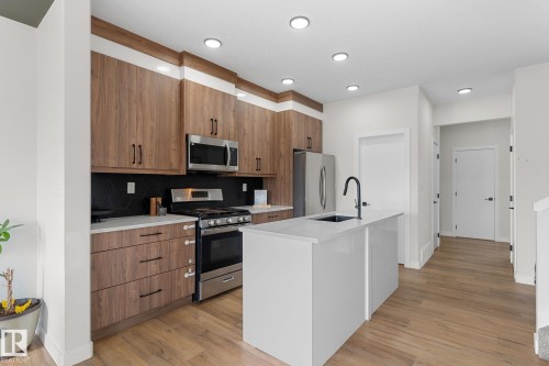 Modern kitchen featuring wood-finish cabinetry, stainless steel appliances, a white island with an undermount sink, recessed lighting, and wood-finish flooring - 1142 Goldfinch Crescent Nw, Edmonton, AB 