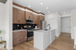Modern kitchen featuring wood-finish cabinetry, stainless steel appliances, a white island with an undermount sink, recessed lighting, and wood-finish flooring - 