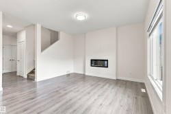Contemporary living space featuring wood-finish flooring, a built-in electric fireplace, a staircase with carpeting, and a window with a roller blind - 
