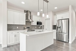 White cabinetry with stainless steel appliances, a center island, grey subway tile backsplash, and wood-finish flooring - 