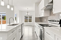 White shaker cabinetry, stainless steel appliances, grey subway tile backsplash, white countertops, and wood-finish flooring - 