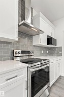 Stainless steel range, white cabinetry, integrated microwave, gray subway tile backsplash, and light-toned countertops - 