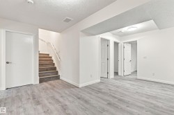 Wood-finish flooring throughout, bright white walls, recessed ceiling light, wood staircase with white railing, and multiple paneled interior doors - 
