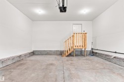 Spacious garage featuring a concrete floor, painted white walls, built-in wooden stairs, and overhead lighting - 