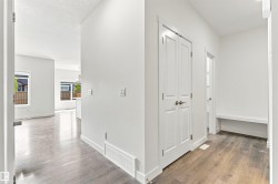 Light wood-finish flooring, white walls, built-in coat closet, recessed wall bench, and white trim throughout - 