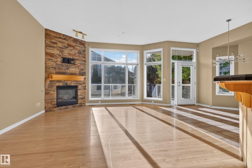 Floor-to-ceiling stone fireplace with a wood mantel, expansive windows, wood-finish flooring, and a glass-paneled exterior door - 876 Twin Brooks Close Nw, Edmonton, AB 