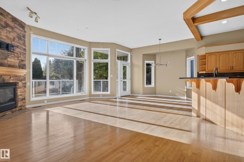 Open-concept living space featuring wood-finish flooring, floor-to-ceiling windows, a full-height stone fireplace surround, and a tiered breakfast bar with cabinetry - 876 Twin Brooks Close Nw, Edmonton, AB 