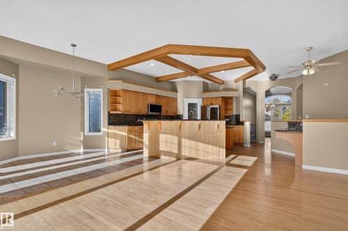 Open-concept floor plan featuring wood-finish flooring, geometric ceiling beams, custom cabinetry, and a central island with countertop seating - 876 Twin Brooks Close Nw, Edmonton, AB 
