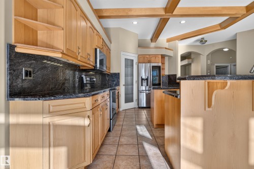 Kitchen featuring light-finish cabinetry, dark stone countertops, tile flooring, exposed ceiling beams, and a pantry with a glass-panel door - 876 Twin Brooks Close Nw, Edmonton, AB 