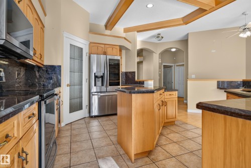 Kitchen featuring light-finish cabinetry, dark stone-surface countertops, stainless steel appliances, a center island with built-in storage, and ceiling beam detailing - 876 Twin Brooks Close Nw, Edmonton, AB 