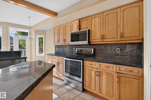 Kitchen featuring natural wood cabinetry, stone countertops, central island, stainless steel appliances, and ceramic tile flooring - 876 Twin Brooks Close Nw, Edmonton, AB 
