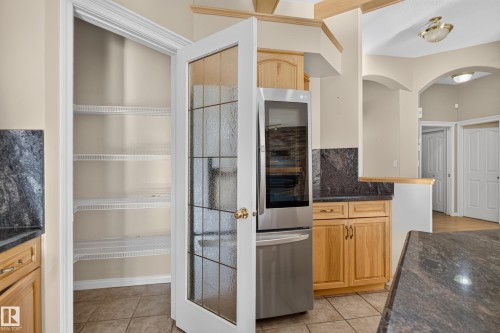 Walk-in pantry featuring white wire shelving and a glass-paneled door, paired with cabinetry, dark stone-finish countertops, tile flooring, and arched architectural detailing - 876 Twin Brooks Close Nw, Edmonton, AB 