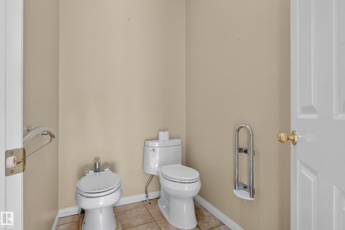 White porcelain toilet, bidet, and wall-mounted metal support rails, complemented by neutral tile flooring - 876 Twin Brooks Close Nw, Edmonton, AB 
