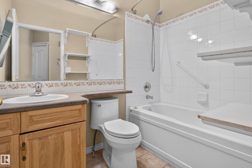 Bathroom featuring wood-finish cabinetry, an oval drop-in sink, solid surface countertop, tiled shower surround, and built-in wall shelving - 876 Twin Brooks Close Nw, Edmonton, AB 