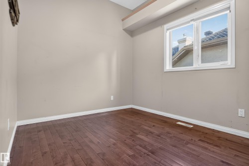 Room featuring wood-finish flooring, neutral-toned walls, vaulted ceiling, and a large window with roller shades - 876 Twin Brooks Close Nw, Edmonton, AB 