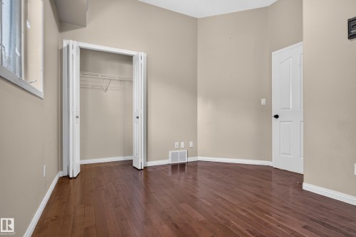 Neutral-toned walls featuring wood-finish flooring, a built-in closet with double-hinged doors, and a paneled interior door - 876 Twin Brooks Close Nw, Edmonton, AB 