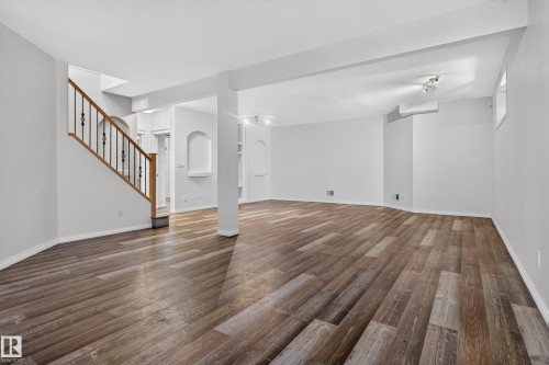 Open-concept space featuring wood-finish flooring, built-in arched wall niches, and a staircase with stained wood handrails and metal balusters - 876 Twin Brooks Close Nw, Edmonton, AB 