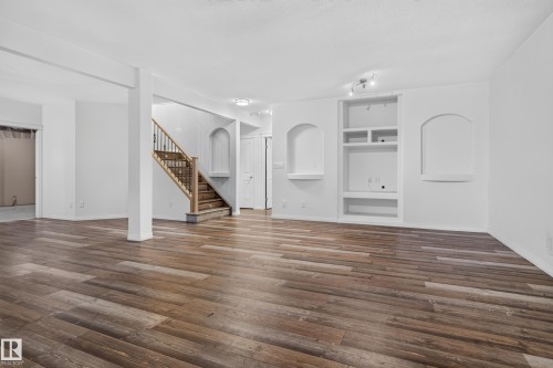 Open interior featuring wood-finish flooring, built-in shelving with arched niches, and a wooden staircase with iron balusters - 876 Twin Brooks Close Nw, Edmonton, AB 