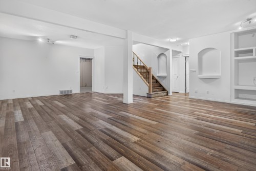 Open-concept space featuring wood-finish flooring, a wooden staircase with metal balusters, built-in recessed shelving, and arched wall niches - 876 Twin Brooks Close Nw, Edmonton, AB 