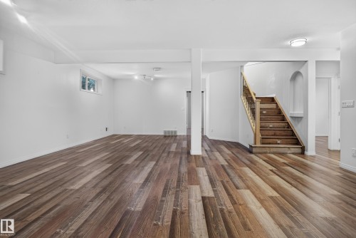 Open floor plan featuring wood-finish flooring, recessed ceiling lighting, a structural support column, and a staircase with a wooden handrail and metal balusters - 876 Twin Brooks Close Nw, Edmonton, AB 