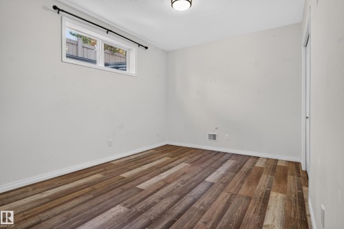 Interior room featuring wood-finish flooring, a neutral wall color palette, a horizontal window with a black curtain rod, and a flush-mount ceiling light fixture - 876 Twin Brooks Close Nw, Edmonton, AB 