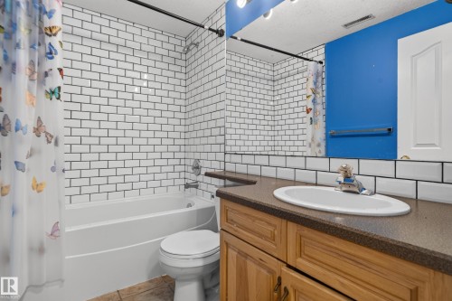Bathroom featuring a tub-shower combination with white subway tile surround, vanity with a dark solid-surface countertop and integrated oval basin, and a wall-to-wall mirror - 876 Twin Brooks Close Nw, Edmonton, AB 