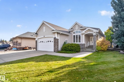 Single-story residence featuring horizontal lap siding, stacked stone accents, an arched window with transom, a covered entryway, and a paved driveway - 876 Twin Brooks Close Nw, Edmonton, AB 