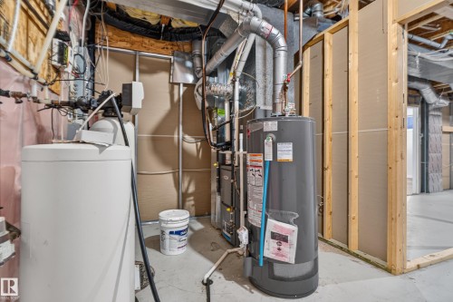 Mechanical area featuring a hot water tank, forced air furnace system, and water treatment unit, set within an unfinished space with exposed framing and concrete flooring - 876 Twin Brooks Close Nw, Edmonton, AB 
