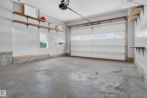 Garage featuring a white paneled overhead door with upper glass inserts, concrete flooring, wall-mounted wood shelving, and a singular window - 876 Twin Brooks Close Nw, Edmonton, AB 