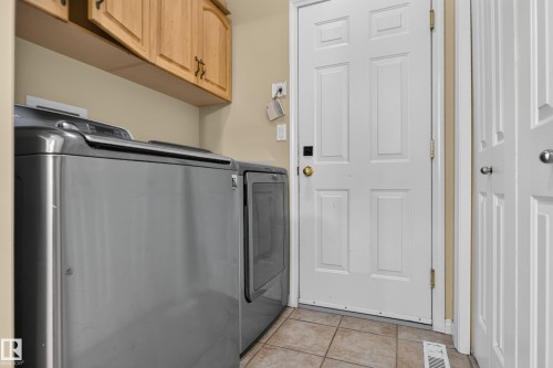 Dedicated laundry area featuring light wood-finish wall-mounted cabinetry, tile flooring, and six-panel interior doors - 876 Twin Brooks Close Nw, Edmonton, AB 