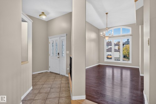 Foyer featuring ceramic tile flooring, a white front door with decorative glass inserts, vaulted ceilings, dark wood-finish flooring, and a multi-light chandelier - 876 Twin Brooks Close Nw, Edmonton, AB 